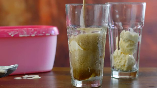 Preparing black cow cola ice cream soda floats against rustic wood background.