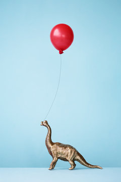 Toy dinosaur and balloon against blue background