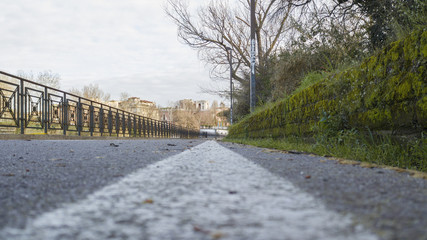 Fototapeta premium View from the bottom of an asphalt road with trees and vegetation on the sides and on the left a railing that separates from the river.