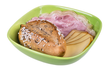 Salty bread roll, slices of ham hock and cheese. The crunchy whole grain bun with sliced pork meat and smoked edam in green bowl. Isolated on white background.