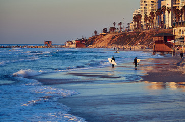 Surfers on the beach of Tel Aviv at sunset.