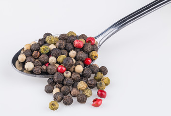 Close-up a spoonful of spicy peppercorns. Piper nigrum. The colorful mix of different pepper corns on the stainless steel spoon partially spilled on a white background.