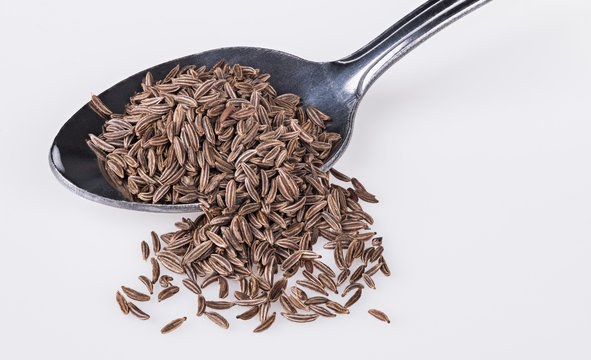 Close-up a spoonful of aromatic caraways. Carum carvi. Pile of brown cumin seeds on the stainless steel spoon partially spilled on a white background. Full depth of field.