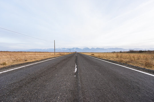 Empty road passing through field against snow-capped mountains 