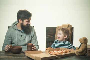 Fototapeta na wymiar Hot pizza slice with melting cheese on a rustic wooden table. Happy family eating pizza while sitting on kitchen at home. Funny family dad and son eating pizza slices for the dinner with smile