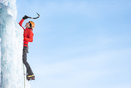 Male ice climber hitting the frozen waterfall with ice axe