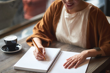 Young woman writing something in the notebook in the cafe