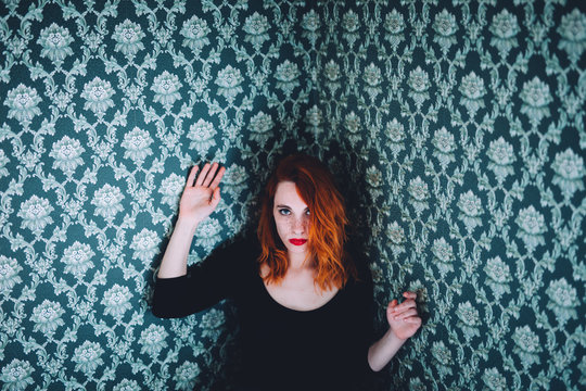 porrait of a ginger woman leaning on a damask wallpaper decorated wall