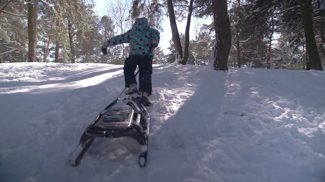 Young adorable boy climbing up the hill with sled during snowy winter time