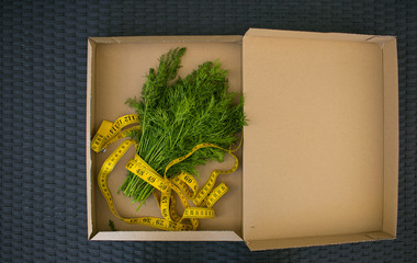 Healthy food and diet concept. Fresh dill bouquet with vegetables and weight and tape measure in the kraft box