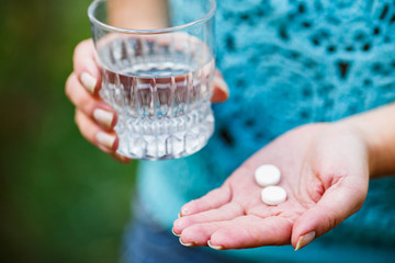 girl holds a glass of clean water and two white pills - obrazy, fototapety, plakaty