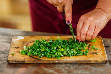female chef cuts fresh green onion for salad