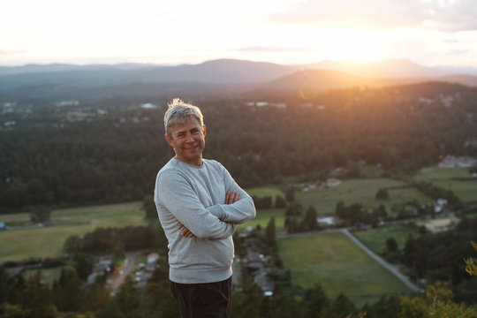 Content grey haired man smiling on hilltop at sunset