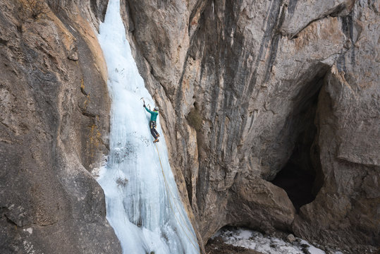 Man climbing on steep frozen waterfall using ice axes
