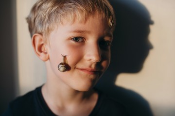 Cute smiling blond boy with snails on his face