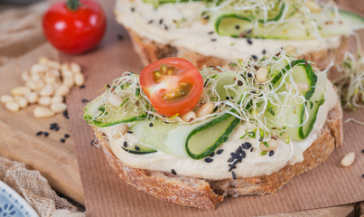 Healthy vegetarian bruschettas with bread, micro greens, hummus, cherry tomatoes, cucumbers and pine nuts