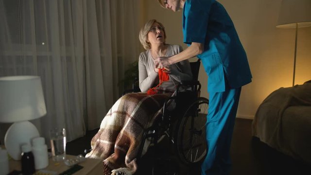 Nurse taking away knitting needles from old woman due to Parkinsons disease