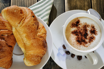Traditional Italian breakfast with cappuccino and croissants on a rustic wooden table