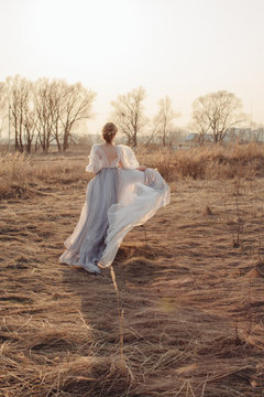 Back view of blond female in beautiful gown run across the field in sunset light