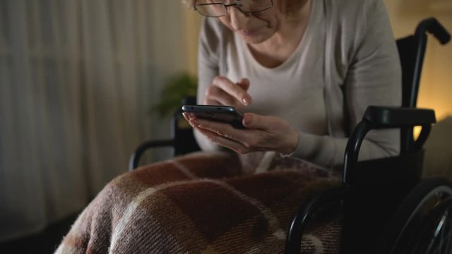 Old woman in wheelchair viewing photos on smartphone, love to grandchildren