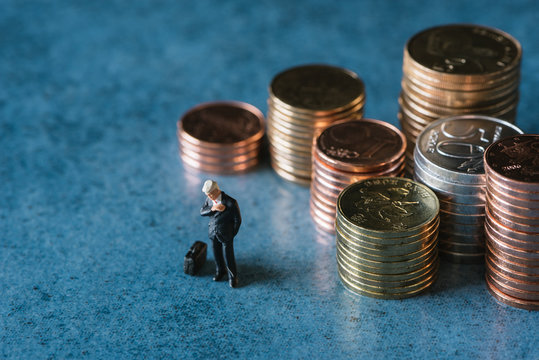 Figurine of businessman checking time near stack of coins