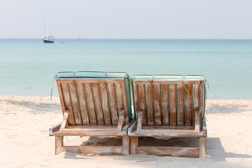 Couple of wooden beach chairs on a tropical sand beach overlooking the sea water and yacht. Thailand
