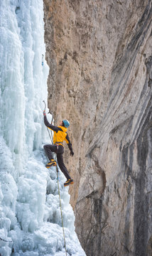 Male alpinist hanging on ice axe climbing on frozen waterfall