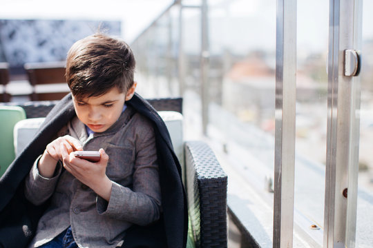 Brunette boy sitting on roof cafe and using smartphone