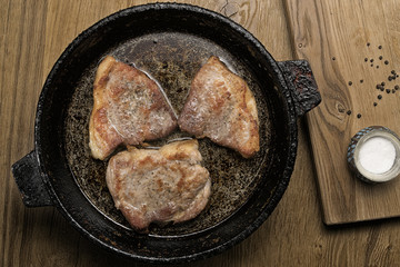 three fried pork steaks in a frying pan