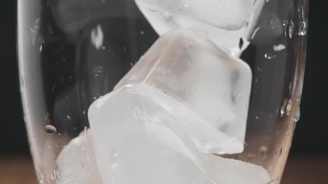 Slow motion closeup pan of ice cubes falling into glass
