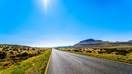 Long Straight Road through the Endless wide open landscape of the semi desert Karoo Region in Free State and Eastern Cape provinces in South Africa under blue sky