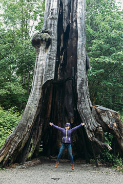Happy woman jump in front of hallow tree trunk