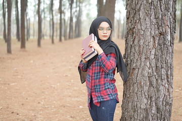 Portrait of happy young muslim woman black hijab and Scottish shirt holding a book in autumn season  background.