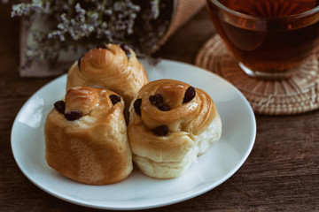 Homemade soft and sticky raisin bread or cinnamon rolls glaze with icing look so delicious on white plate served with hot tea on wood table in vintage tones. Bakery concept for cafe or restaurant.