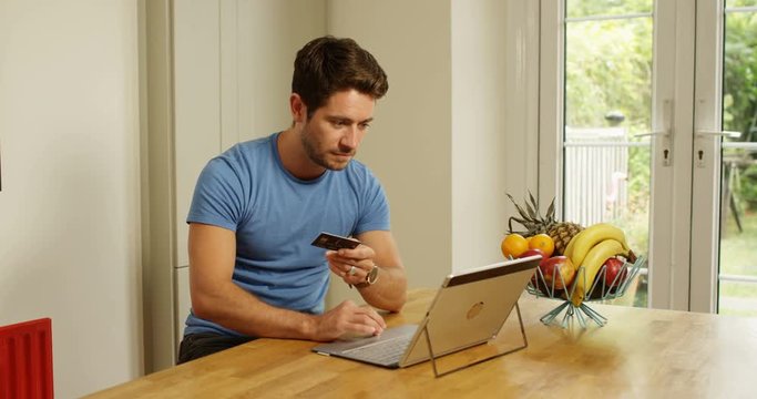 4K Attractive man relaxing at home, shopping online with credit card. Slow motion.