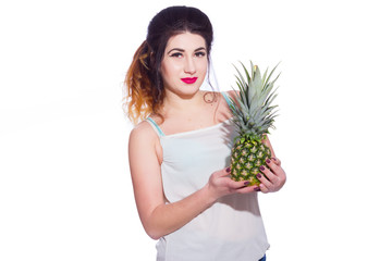 Summer studio portrait of a beautiful young brunette woman with long hair. A girl in a summer T-shirt and jeans is holding a pineapple in her hands. Concept: summer photography and a sunny mood