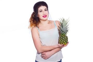 Summer studio portrait of a beautiful young brunette woman with long hair. A girl in a summer T-shirt and jeans is holding a pineapple in her hands. Concept: summer photography and a sunny mood