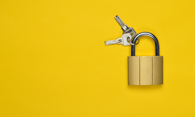 Golden closed lock with keys on a yellow background. Copy space. Top View.