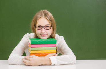Young girl hugs a stack of books on the background of a school board