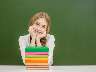 Cute teen girl with books on the background of a school board. Space for text