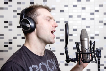 A young guy singer and rock musician sings in a studio condenser microphone in headphones in a...