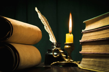 The concept of education and writing, a pen in an inkwell and a candle with a candle and scrolls of...