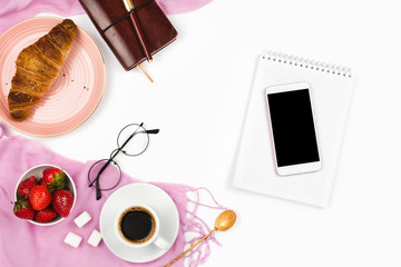 Fototapeta na wymiar Beautiful flatlay arrangement with croissant, cup of coffee, fresh strawberries, smartphone with black copyspace and other business accessories: concept of busy morning breakfast, white background.