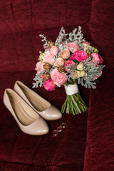 Wedding bouquet with purple and pink roses. Wedding accessories are lying on a red armchair