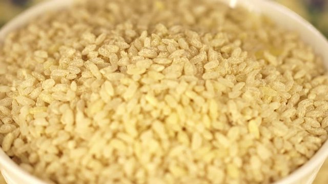 The plate from rice turns around itself on a support. Black background. White dry rice close up. Rice for pilaf. semi-indistinct shot