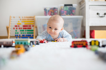 Cute little baby boy, playing with toy cars on the carpet in children room