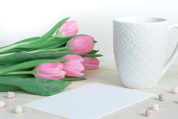 Soft feminine desktop with pink tulips, designer mug and postcard