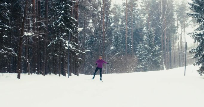 WIDE TRACKING Front view of young adult Caucasian female athlete practicing cross-country skiing on a scenic forest trail. 4K UHD 60 FPS SLO MO
