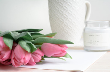 Spring composition with pink tulips and white candle, ceramic mug and card