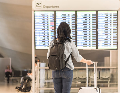 Passenger With Luggage At The Flight Information Board In Airport Terminal Waiting Hall Area Checking Time For Flight Departure-arrival And Delay Status